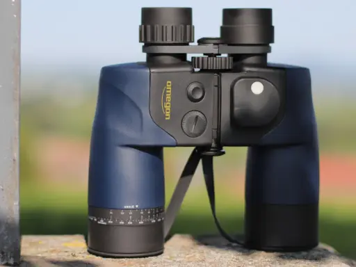 Ein blaues Omegon Fernglas 7x50, dessen Bedeutung in der Vergrößerung und Objektivgröße liegt, steht auf einem Stein.