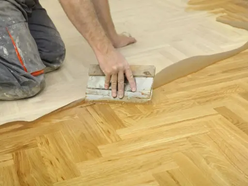 Un artisan applique un produit sur un parquet en chevrons. Une étape essentielle pour la réparation parquet.