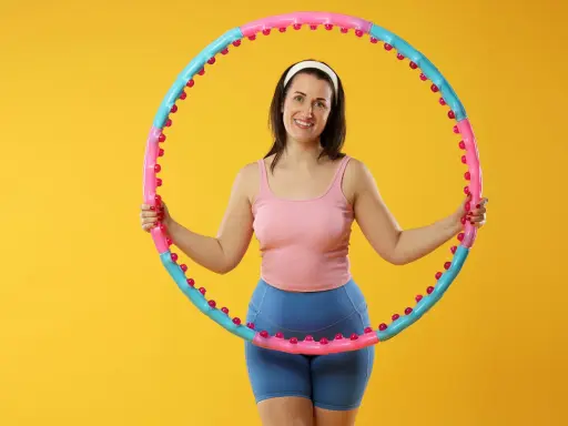 Uśmiechnięta kobieta z hula hop. Dowiedz się, jak dobrać hula hop do wzrostu, by ćwiczenia były efektywne i przyjemne.