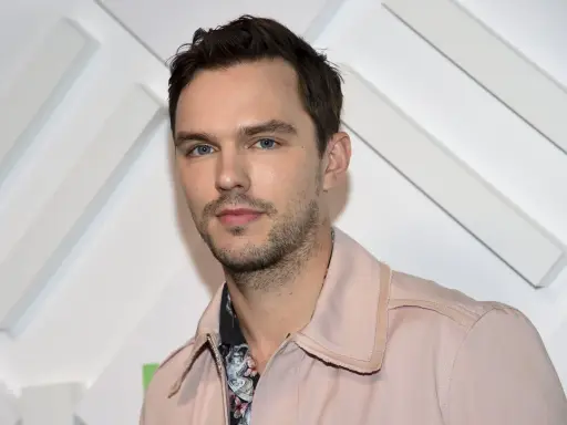 Nicholas Hoult, känd från filmer och tv-program, poserar framför en vit bakgrund med diagonala linjer.