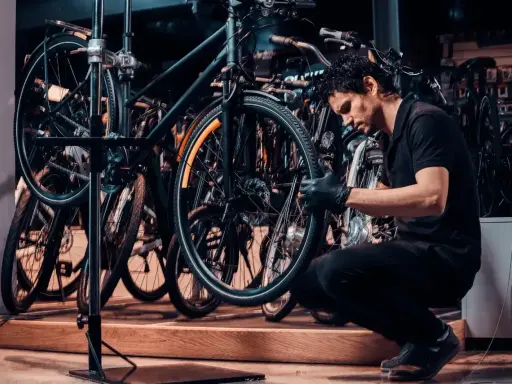 Mechanik w czarnej koszulce i rękawiczkach pokazuje, jak zdjąć tylne koło w rowerze, pracując w serwisie rowerowym.
