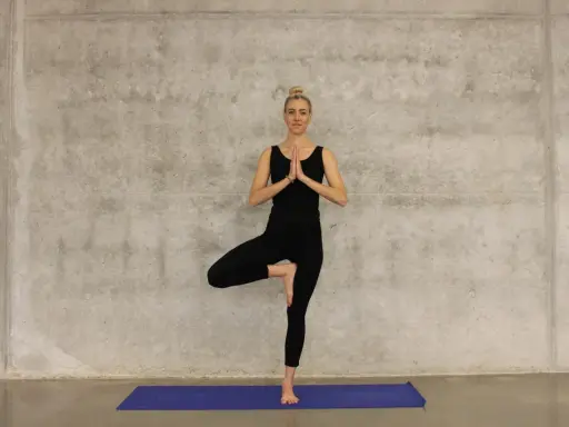 Kvinna i svart träningsklädsel utför trädpositionen, en klassisk yogaövning som passar utmärkt för senior yoga.