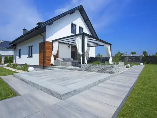 Nowoczesny taras z szarego betonu, z pergolą i meblami ogrodowymi. Idealne miejsce na relaks.