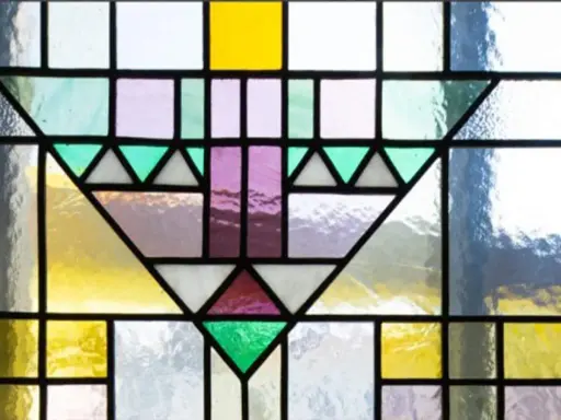 Un motif géométrique coloré orne cette fenêtre vitraux, mêlant le jaune vif, le violet doux et le vert émeraude.
