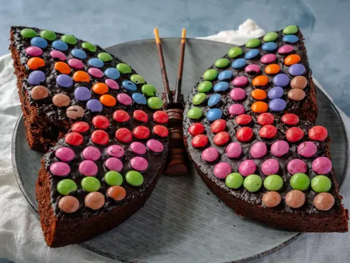 Ein schokoladiger Smarties Kuchen in Form eines Schmetterlings, der mit bunten Smarties dekoriert ist.