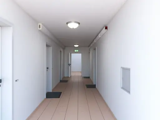 Ein langer, heller Flur mit mehreren Türen und einem grünen Notausgangsschild. Dieser notwendiger Flur ist gut beleuchtet und wirkt einladend.