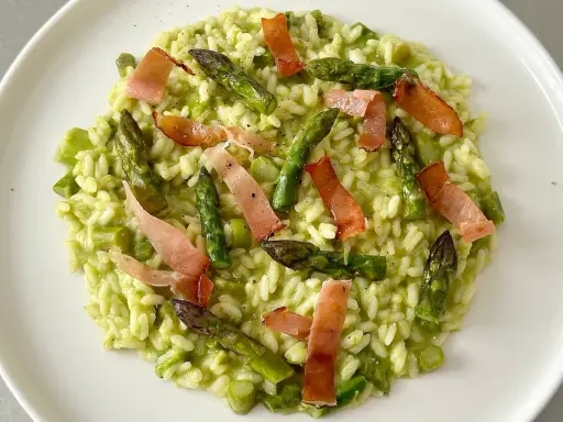 Risotto cremoso con asparagi freschi e croccanti strisce di speck, un piatto primaverile che delizia il palato.