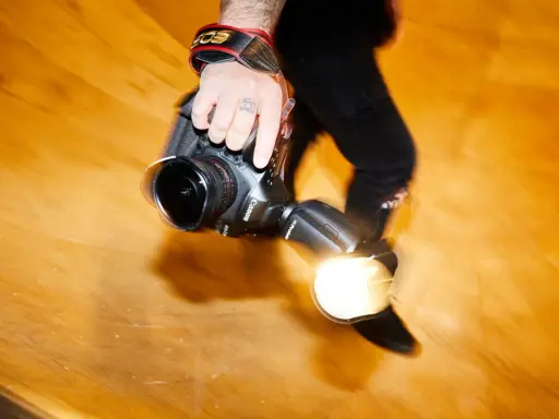 Dłoń fotografa trzyma aparat z lampą błyskową. Długi czas naświetlania tworzy efekt ruchu.