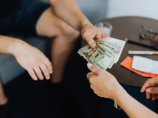 Dwie osoby przekazują sobie plik banknotów. Scena sugeruje nielegalną transakcję, być może korupcję.