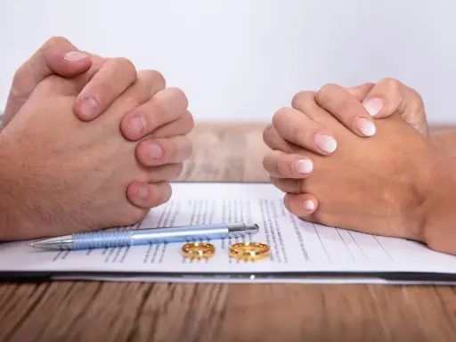 Dwie pary splecione dłonie nad dokumentem, na którym leżą obrączki i długopis. Może to symbolizować trudne decyzje, jak kredyt przed ślubem.