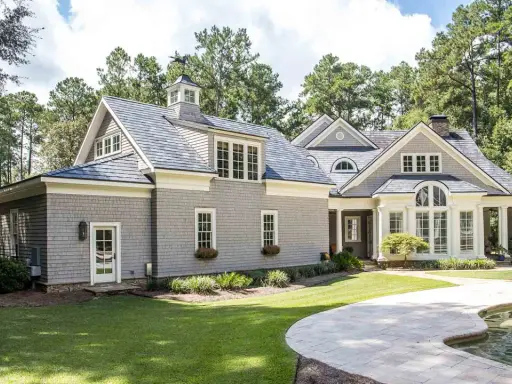 Ein schönes Haus im amerikanischen Stil mit grauer Schindelfassade, großen Fenstern und einem gepflegten Garten mit Pool.