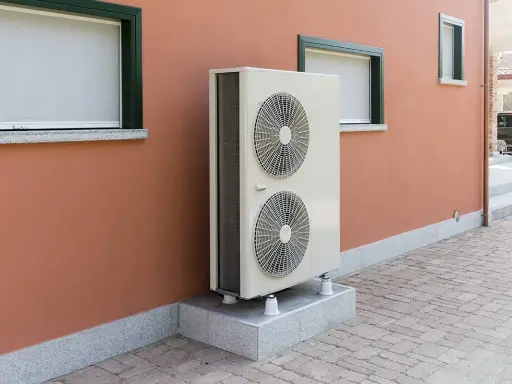 Unité extérieure d'une pompe à chaleur, installée sur un socle devant un mur de maison. Ce système contribue à réduire le cout aerothermie.