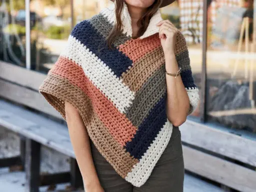 Mujer con un poncho de ganchillo a rayas en tonos tierra, azul marino y blanco. El patrón poncho es ideal para el otoño.