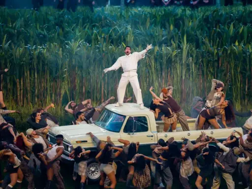 Super Bowl-artister dansar runt en pickup bland majsstjälkar. En artist står på taket.