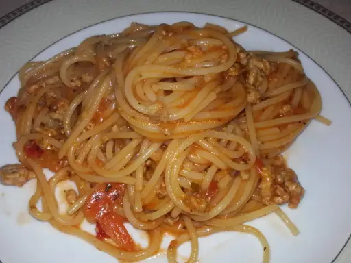 Pyszne spaghetti bolognese z passaty, z mielonym mięsem i kawałkami pomidorów, podane na białym talerzu.