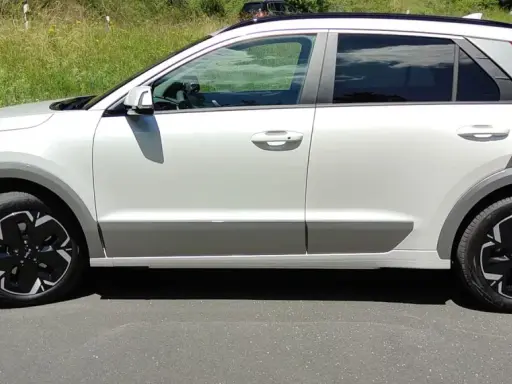 Biały Kia Niro EV z czarnymi felgami stoi na drodze, otoczony zielenią.