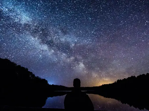 Zachwycająca fotografia astronomiczna Drogi Mlecznej nad jeziorem. Sylwetka człowieka kontempluje kosmos.