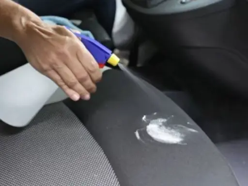 Mano rocía un asiento de coche con un limpiador para eliminar manchas de flujo.