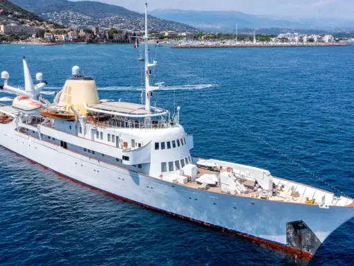 Die Christina O., eine luxuriöse Yacht, gleitet auf dem azurblauen Meer vor einer Küstenstadt.