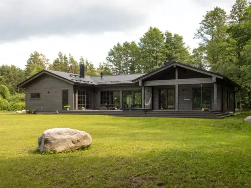 Ein modernes Architektenhaus aus Holz, eingebettet in üppiges Grün. Große Fensterfronten und eine Terrasse laden zum Entspannen ein.