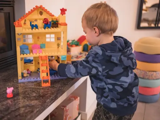 Kleiner Junge spielt mit einem Puppenhaus. Ein Schritt beim **Kinderzimmer ausmisten** ist, Spielzeug zu sortieren.