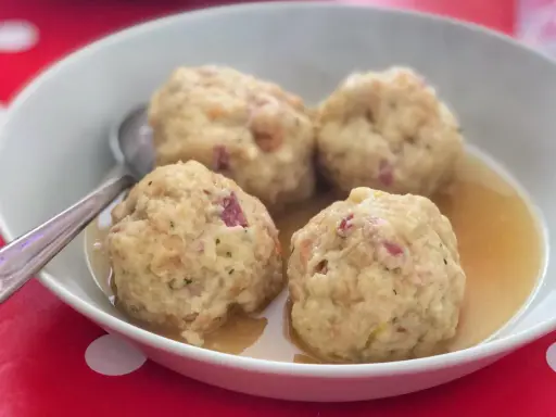 Canederli in brodo, uno dei piatti tipici del Trentino Alto Adige, serviti in una ciotola bianca su un tovagliolo rosso a pois bianchi.