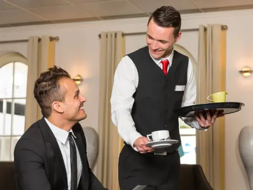 Un serveur souriant présente une tasse de café à un client, illustrant le protocole de service à table.