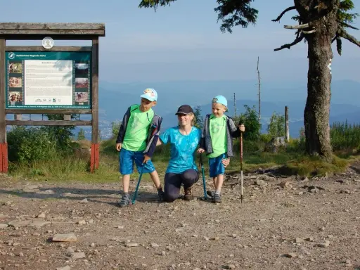 Rodzina na szczycie Baraniej Góry. Dzieci z kijkami trekkingowymi, mama klęczy obok.