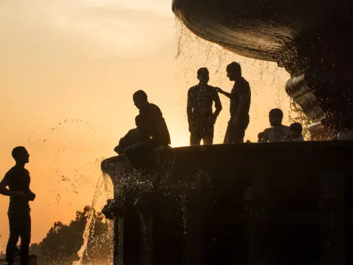 Silhouette fotografia di persone che si rinfrescano in una fontana al tramonto, con l'acqua che scintilla contro il cielo arancione.