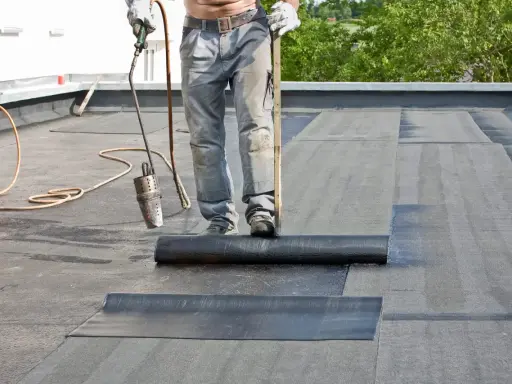 Dachdecker verlegt mit Brenner und Rolle Bitumenbahnen auf einem Flachdach.