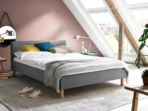 En mysig säng med kuddar i olika färger, en filt med fransar och en spegel på väggen. Frågan är hur litet får ett sovrum vara?