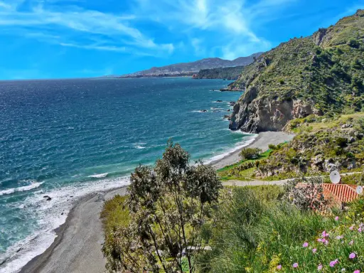 Ein malerischer granada strand mit felsigen Klippen, türkisfarbenem Meer und einer Stadt am Horizont.