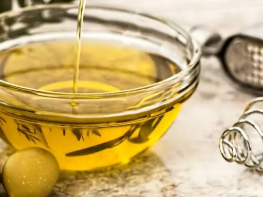 Aceite de oliva vertiéndose en un bol de cristal, rodeado de aceitunas. Varios tipos de aceite comestible para cocinar.
