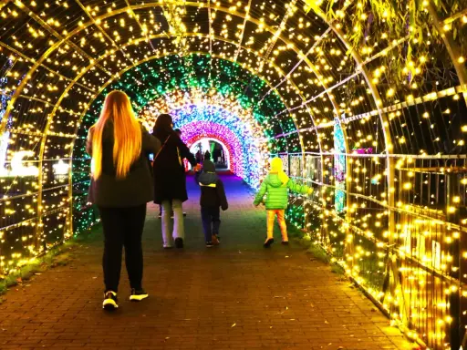 Rodzina spaceruje przez świetlisty tunel w Krakowie. Kolorowe lampki tworzą magiczny ogród świateł.