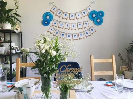 Urocze dekoracje na chrzest diy: girlanda "Chrzest Święty", bukiety białych kwiatów i ozdobne napisy.