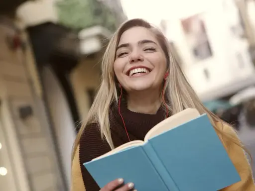 Uśmiechnięta dziewczyna z książką i słuchawkami na ulicy. Może to być studentka, która właśnie skończyła lekcje w szkole w Danii.