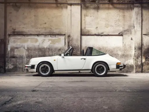 Weißer Porsche 911 3.2 Carrera Targa, ein Klassiker mit stabiler Wertentwicklung, steht in einer alten Lagerhalle.