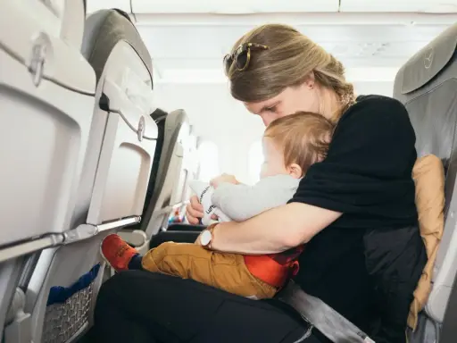 Mama tuli do samolotu z dzieckiem. Siedzą obok siebie, a dziecko bawi się zabawką.
