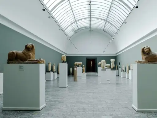 Starożytne rzeźby lwów i popiersi w muzeum w Kopenhadze, podświetlone przez świetlik w dachu.