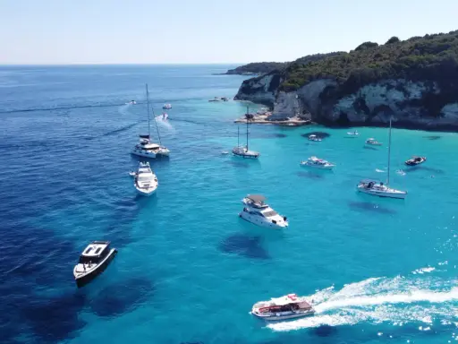 Båtar i turkost vatten vid en klippig kust, en idyllisk vy från Paxos, Grekland.