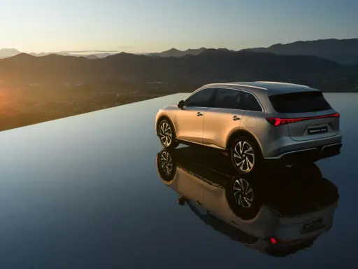El MG6 EV plateado se refleja en una superficie de agua infinita al atardecer, con montañas al fondo.