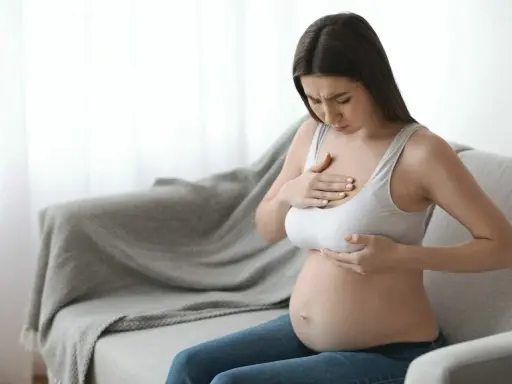 Ciężarna kobieta z bólem dotyka piersi, czując pierwsze oznaki siary.