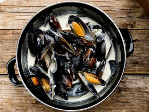 Un plat de moules à la crème, prêtes à être dégustées, sur une table en bois rustique.