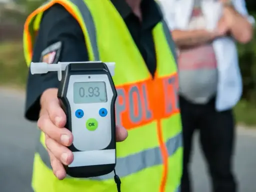 Policjant trzyma alkomat z wynikiem 0.93, pokazując dopuszczalną ilość alkoholu w wydychanym powietrzu.