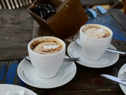 Zwei Tassen Kaffee Latte mit Milchschaum und Kakao-Muster auf einem Holztisch.