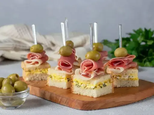 Eleganckie mini przekąski na imprezę: kanapki z szynką, jajkiem i oliwkami na wykałaczkach.