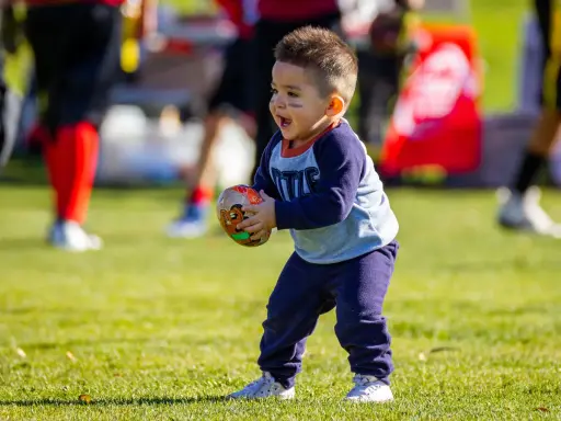 Niño feliz jugando con una pelota de fútbol americano, disfrutando de los juegos con pelotas para niños en un día soleado.