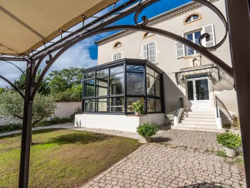 Une élégante véranda moderne s'intègre à une maison de campagne. La surface de plancher pavée mène à des marches menant à la porte d'entrée.
