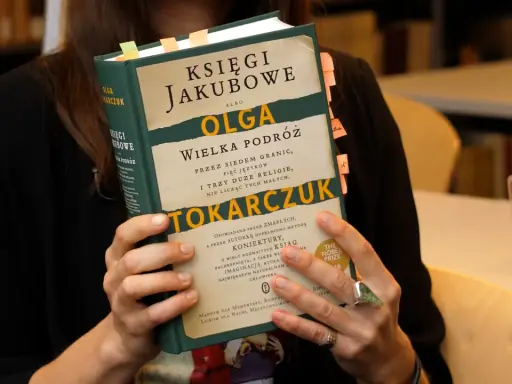 Osoba trzyma książkę "Księgi Jakubowe" Olgi Tokarczuk, z zakładkami w różnych kolorach.