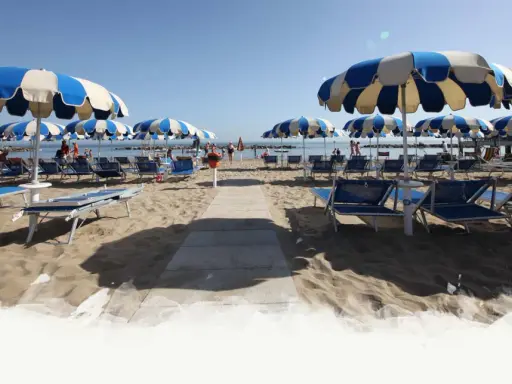 Ombrelloni a righe blu e bianche e lettini preparati per i visitatori al Delfini Beach Village Cattolica, con il mare sullo sfondo.
